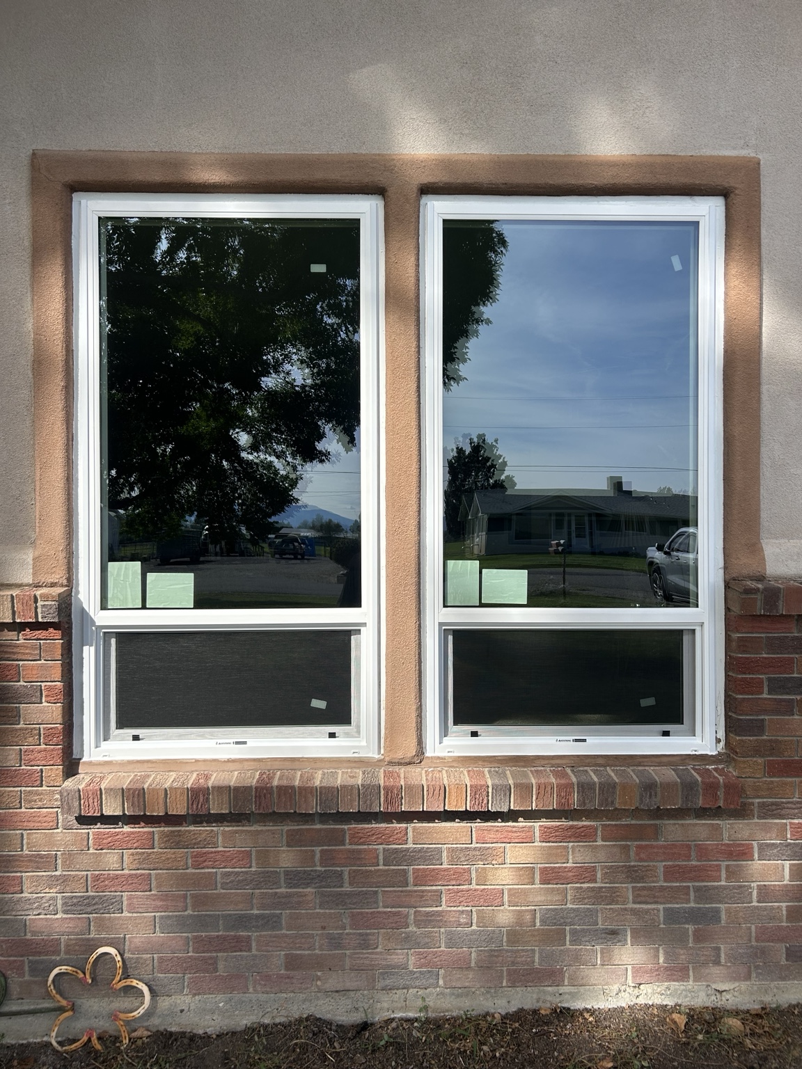 Exterior view of two installed white-framed windows in a brick and stucco wall